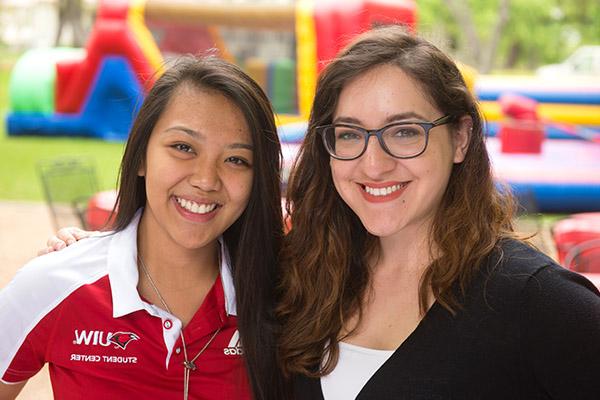 Two female students smiling with campus activities happening in the background